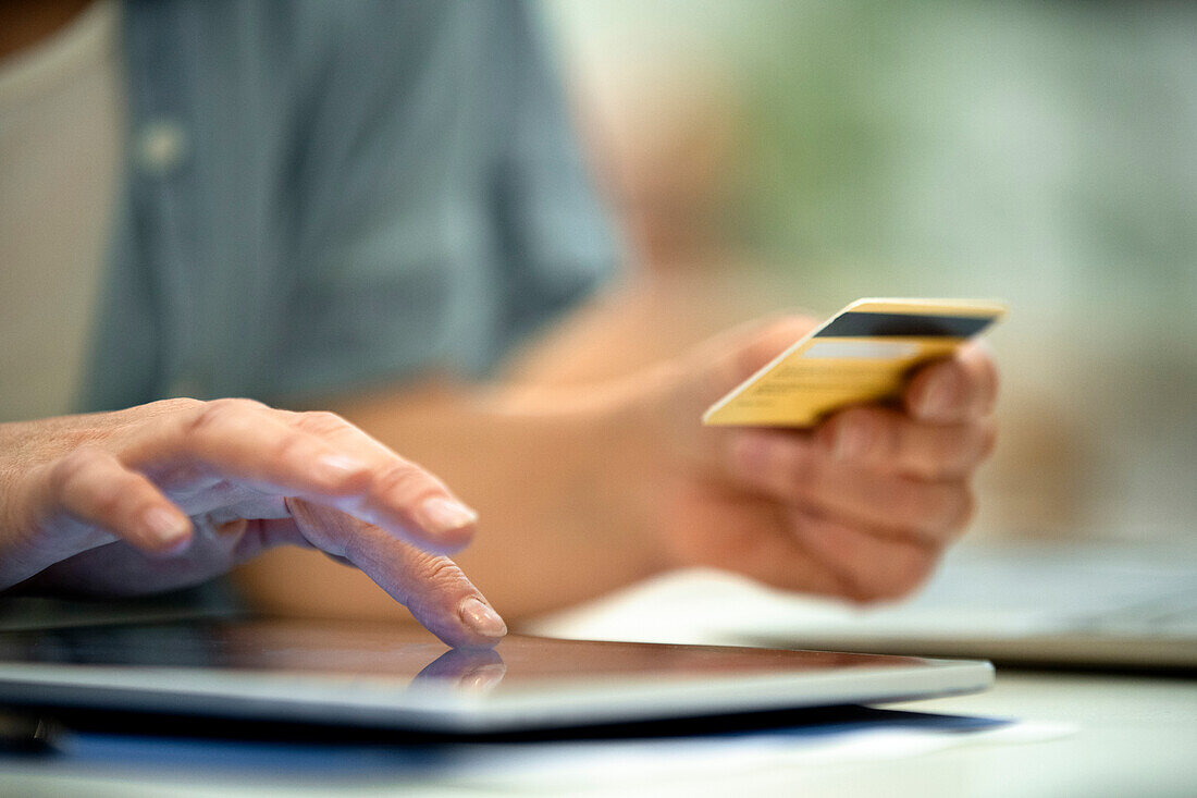 Nahaufnahme der Hände einer erwachsenen Frau beim Bezahlen mit Kreditkarte im Internet