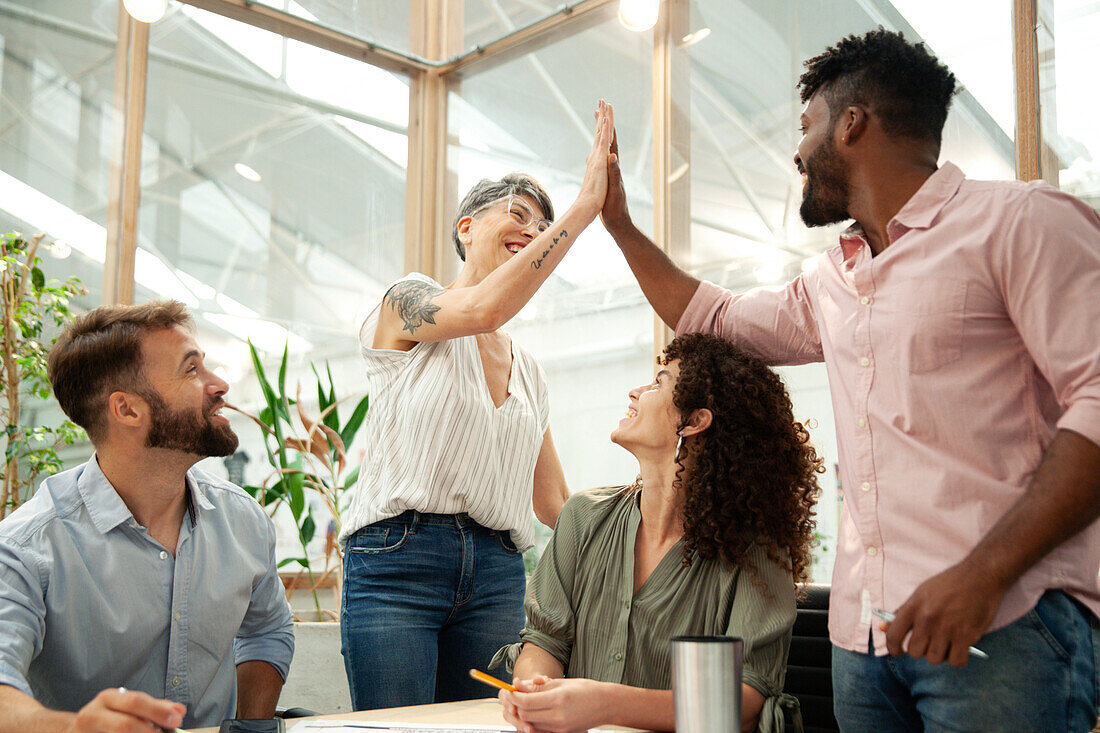 Two coworkers high fiving during project meeting at office