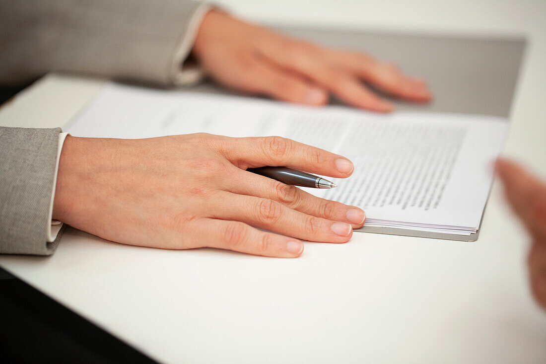 Close-up of woman hands resting on contract while holding a pen