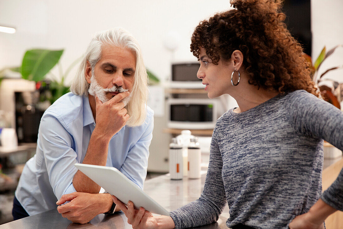 Coworkers leaning on kitchen counter while looking at digital tablet