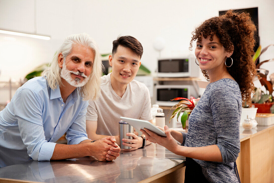 Coworkers looking at the camera while holding digital tablet at office kitchen