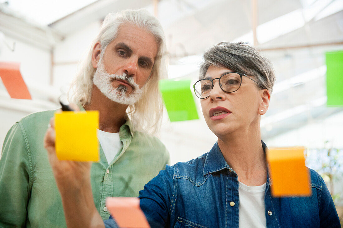 Mid adult female manager writing new ideas on sticky note on glass wall