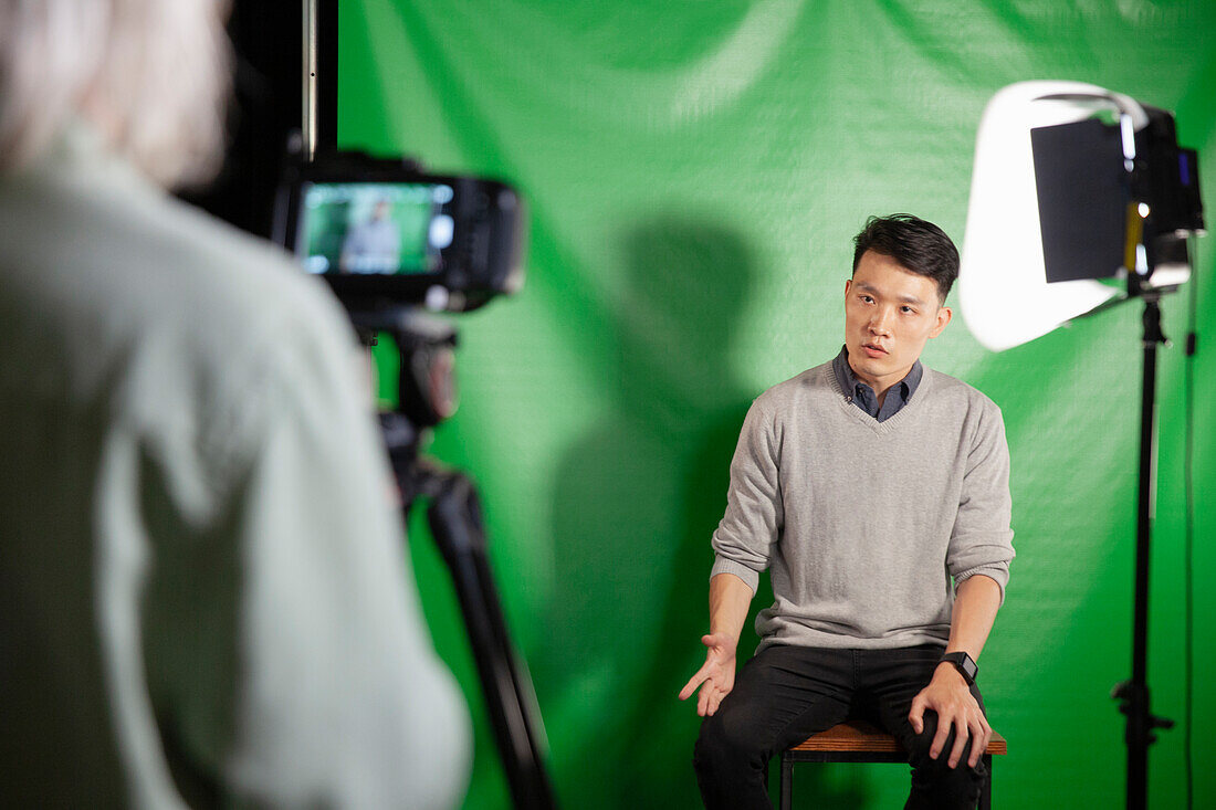 Young adult man giving an interview while sitting against green screen