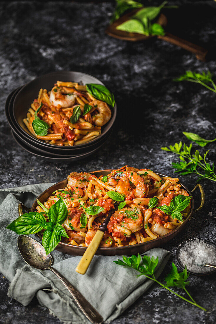 Oval copper bowl with pasta with prawns in red sauce with basil