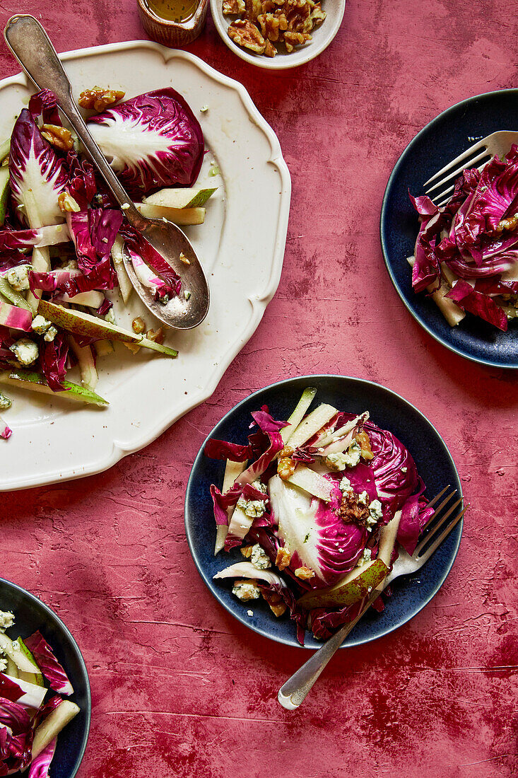 Raddichio, pear, walnut and blue cheese salad on a white oval plate on a pink background, with dressing, with three portions on blue plates