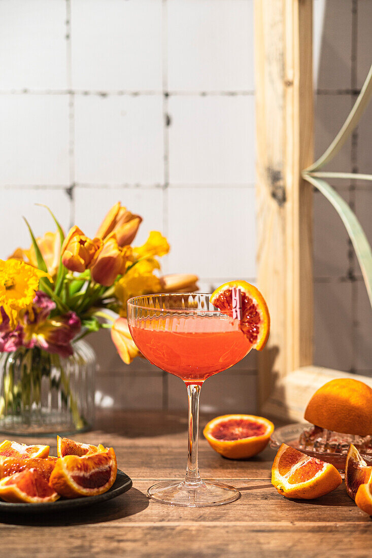 A gin cocktail with blood oranges next to a window