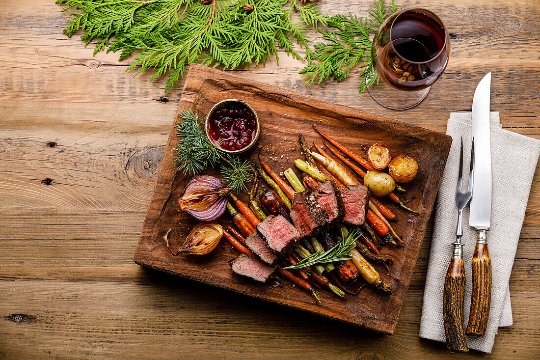 Gegrilltes Hirschsteak mit gebackenem Gemüse, Beerensauce und Rotwein auf Holzuntergrund