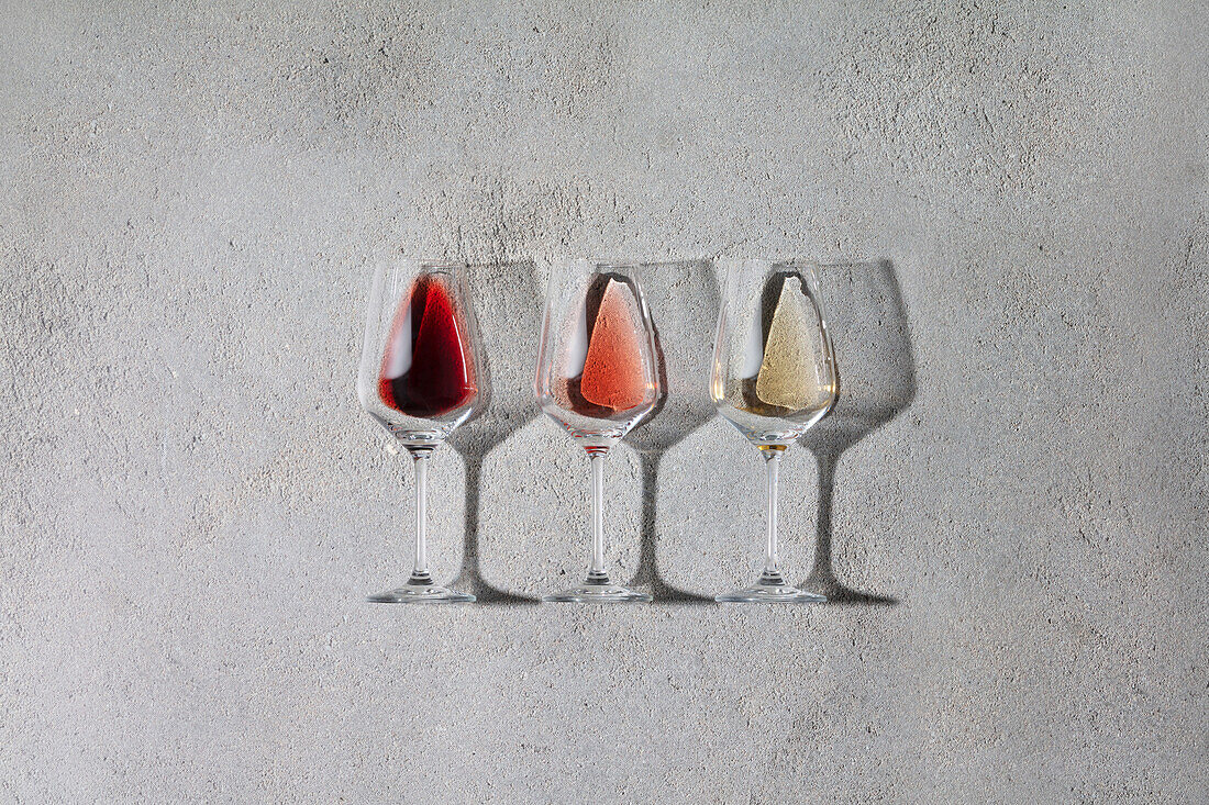 Rot-, Rosé- und Weißwein in Gläsern auf grauem Steinhintergrund. Weinbar, Weingut, Weinverkostung Konzept. Minimalistische trendige Fotografie