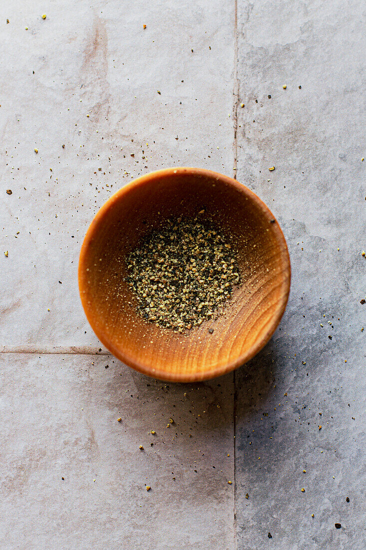 Flatlay of a small bowl of ground black pepper on a tiled surface