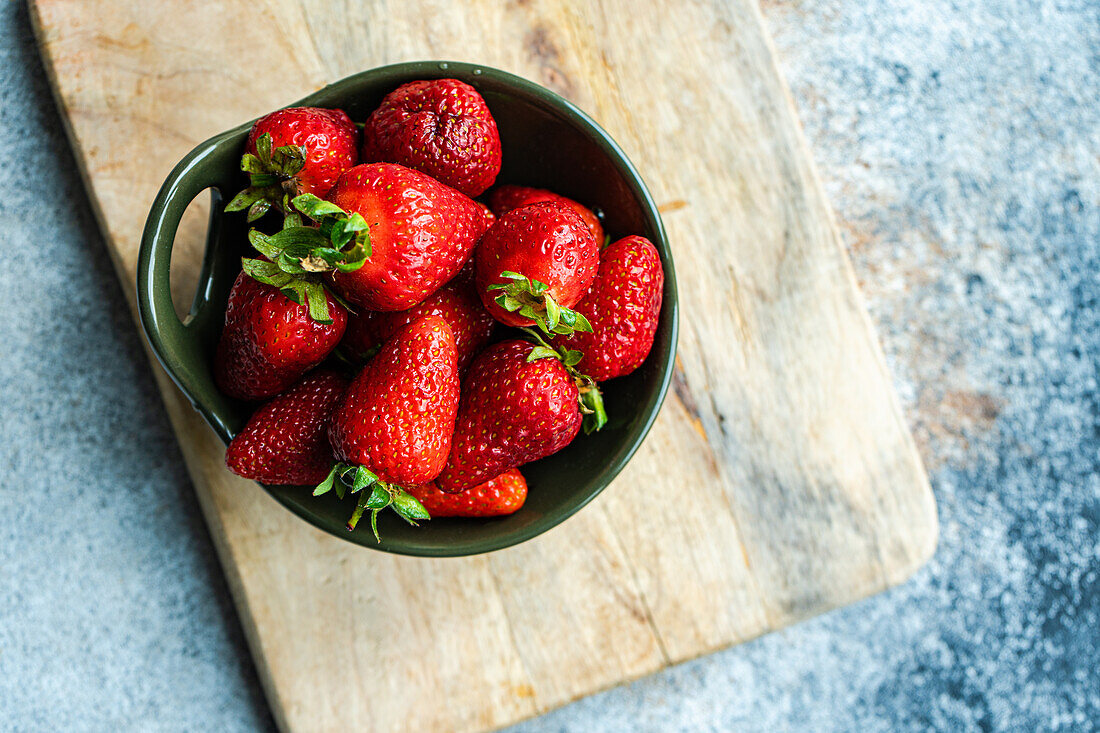 Ripe organic strawberries in ceramic bowl on concrete background