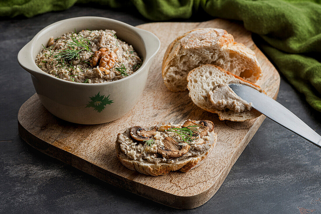 A bowl of mushroom pâté, a sandwich and a piece of bread on a chopping board