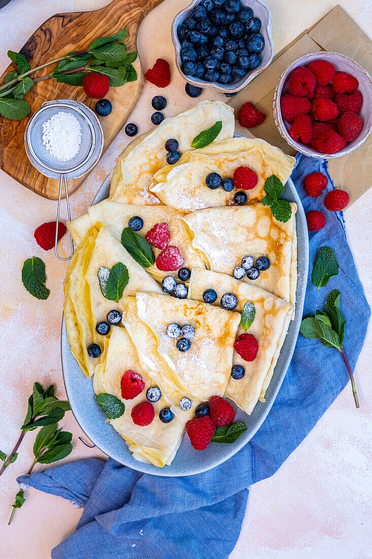 Crepes mit Himbeeren, Heidelbeeren und frischer Minze auf einem großen ovalen Teller