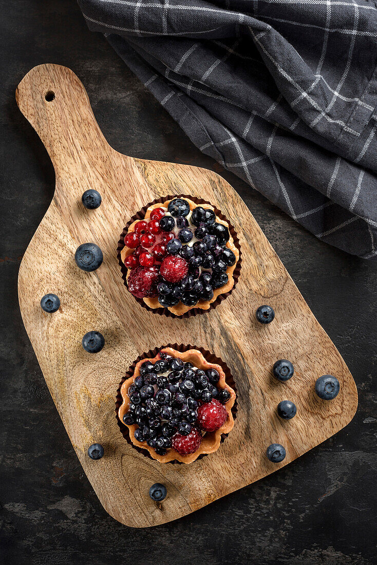 Gebäckkörbchen mit Blaubeeren und Himbeeren. Torten auf einem Schneidebrett. Ansicht von oben