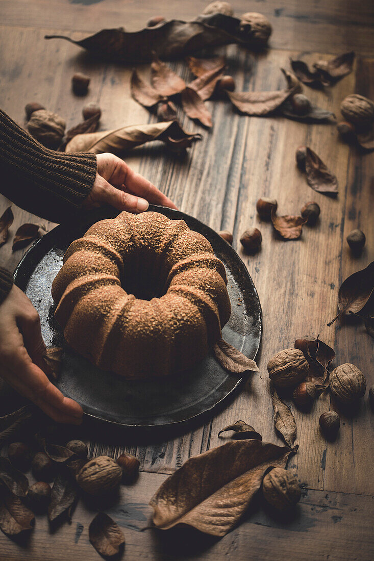 Bundt cake on a wooden table, held in the hands of a woman