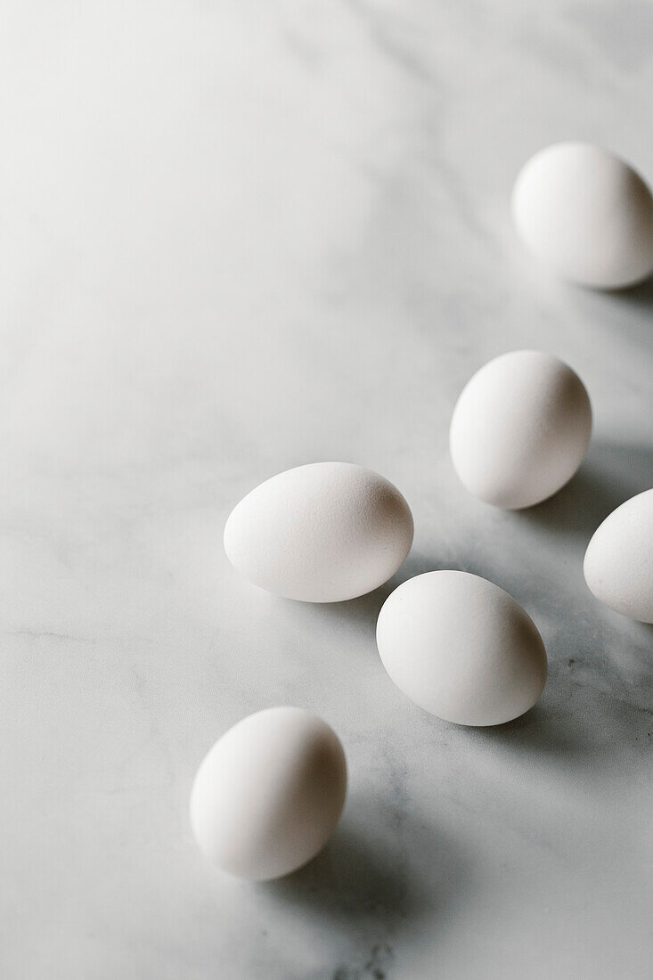 A group of fresh eggs on a white marble surface.