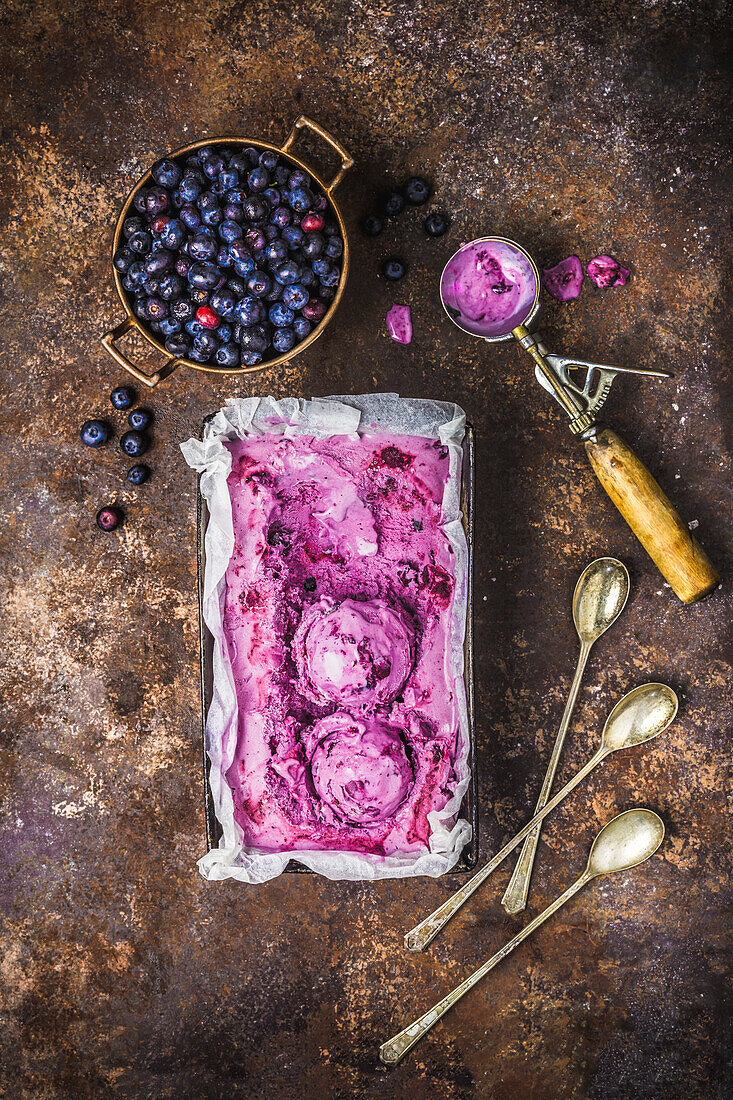 Blueberry ice cream in vintage tin with fresh blueberries in copper colander and antique scoop and dessert spoons