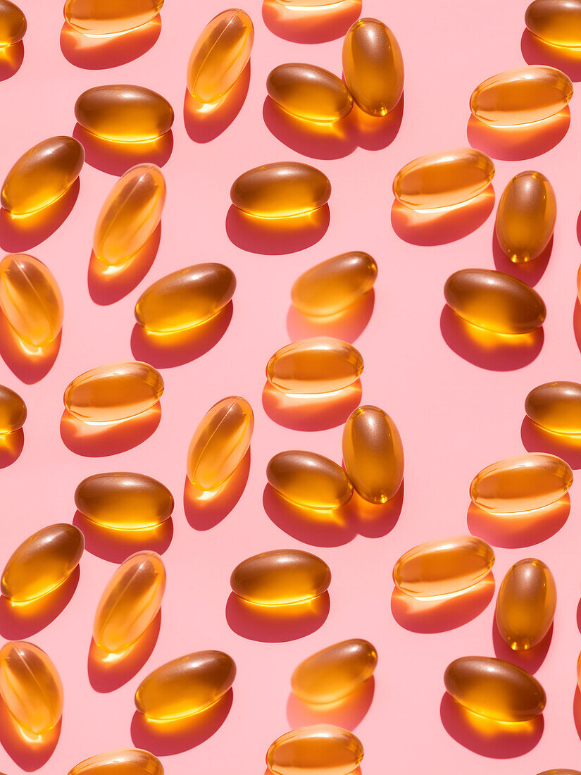 Top view composition of orange vitamin pills scattered on pink background in light studio