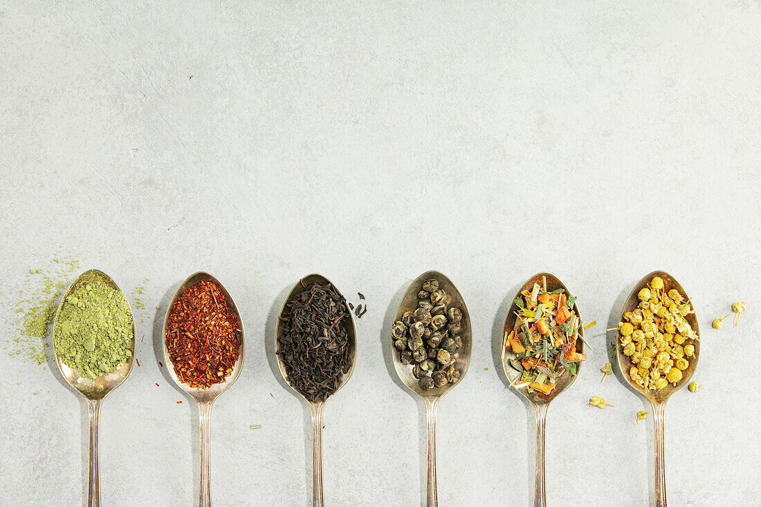 Different types of tea in vintage spoons. Flat lay, top view on concrete background. Matcha, rooibos, black, green, herbal mix and camomile tea. Copy space