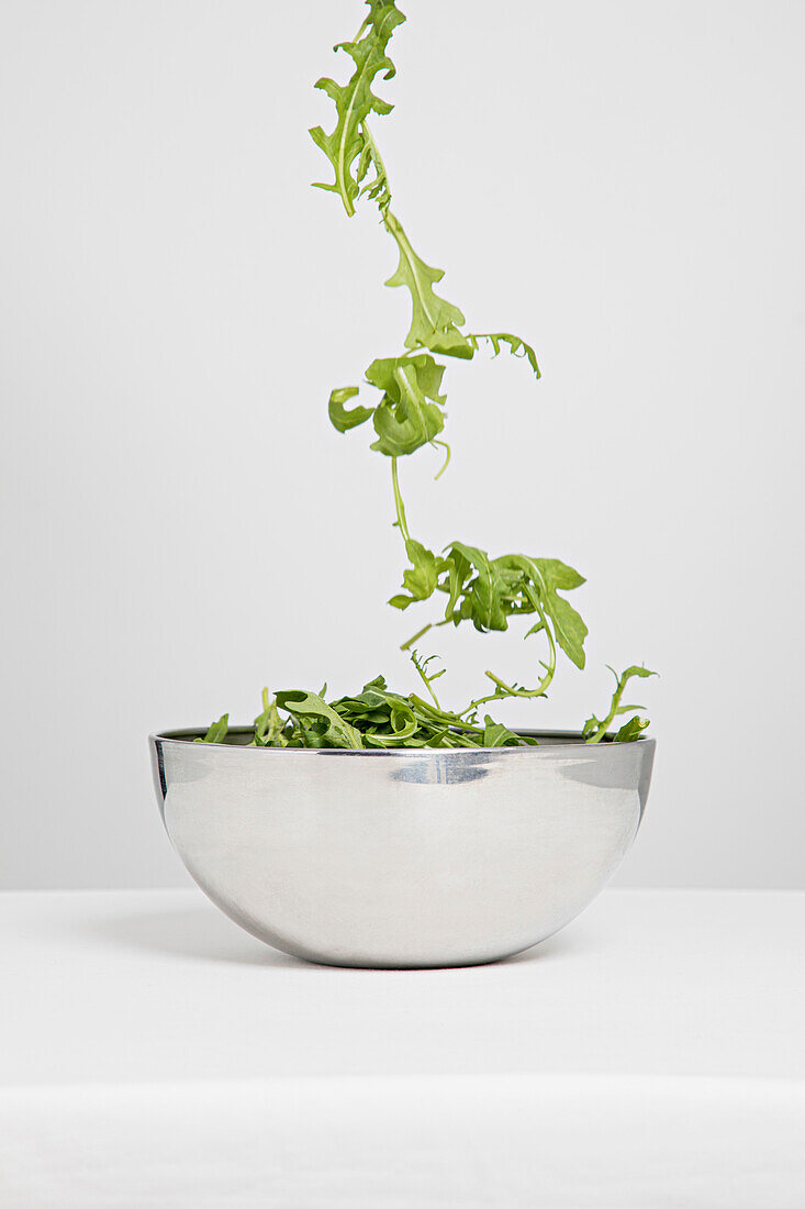 Salad falls into a silver bowl