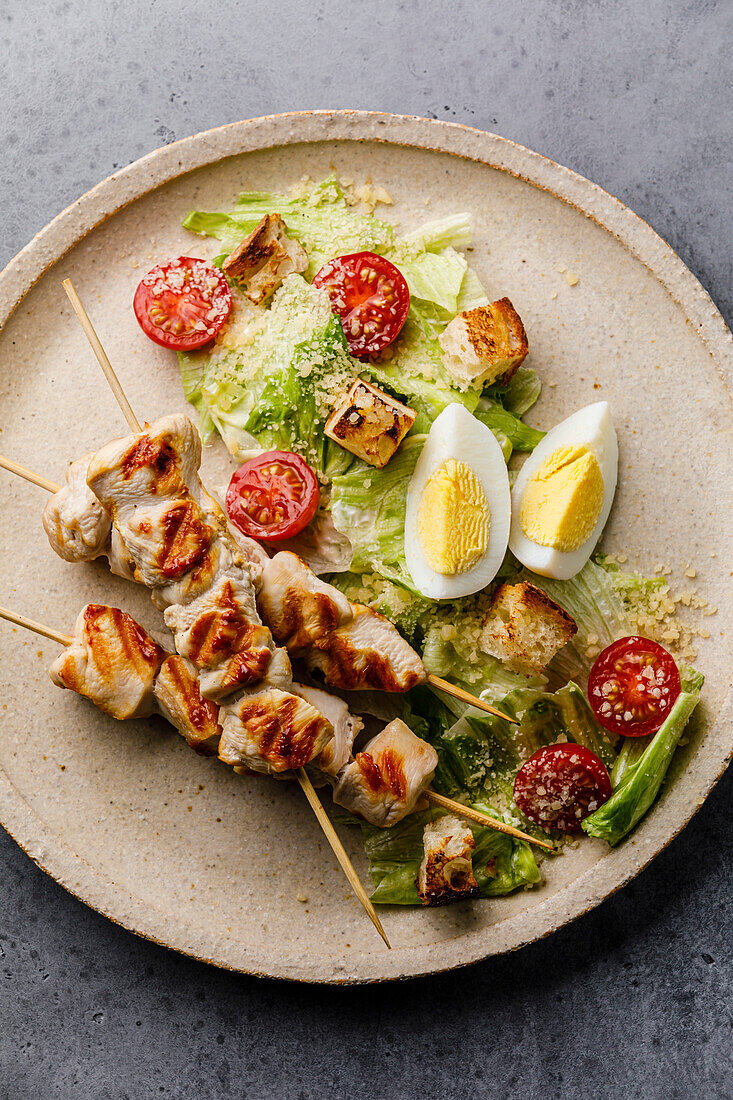 Caesar salad with chicken breast on a skewer and egg on a plate