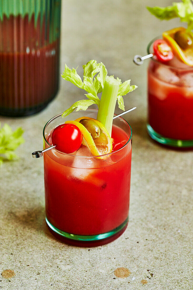 Bloody Mary cocktail with celery, tomato and olive garnish on a sage green background