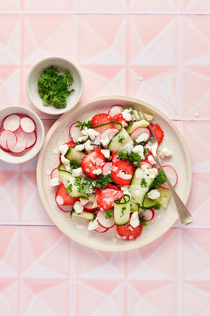 Frühlingssalat mit Erdbeeren, Gurken, Rettich und Petersilie auf rosa Kacheln