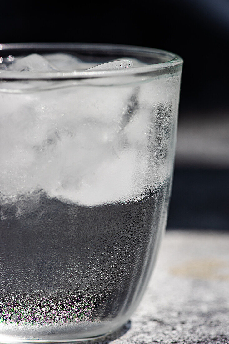 Nahaufnahme eines Glases mit reinem Wasser und Eiswürfeln an einem heißen Sommertag