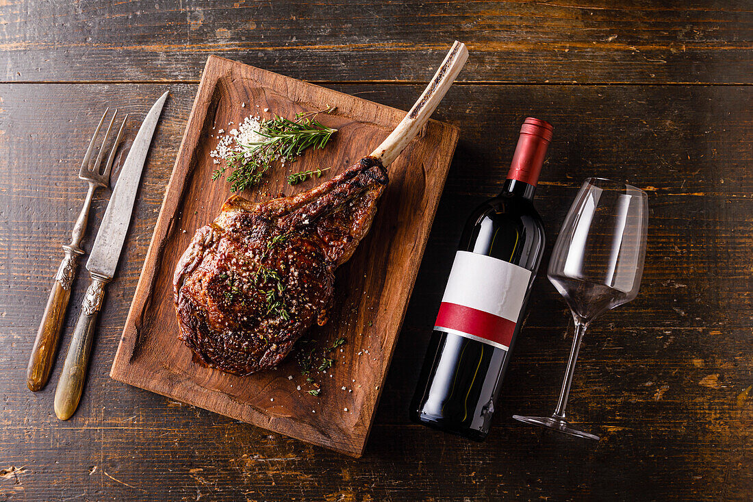Gegrilltes Tomahawk Steak am Knochen und eine Flasche Rotwein auf einem hölzernen Hintergrund