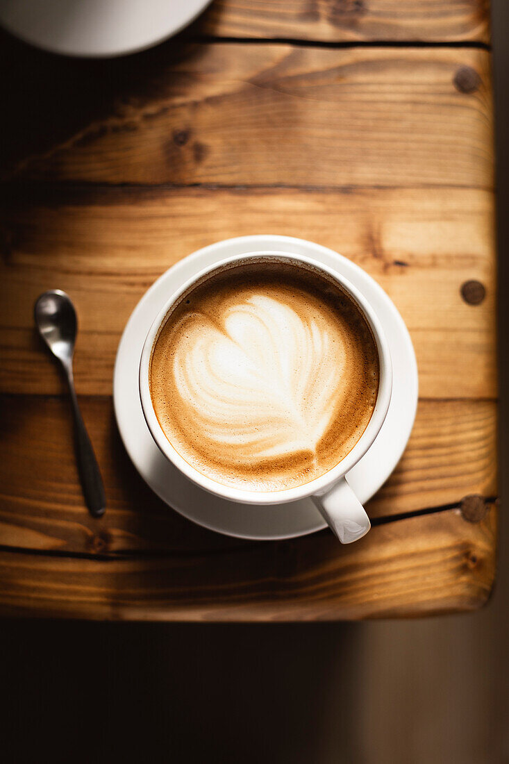 Coffee in white cup on wooden table, with spoon.