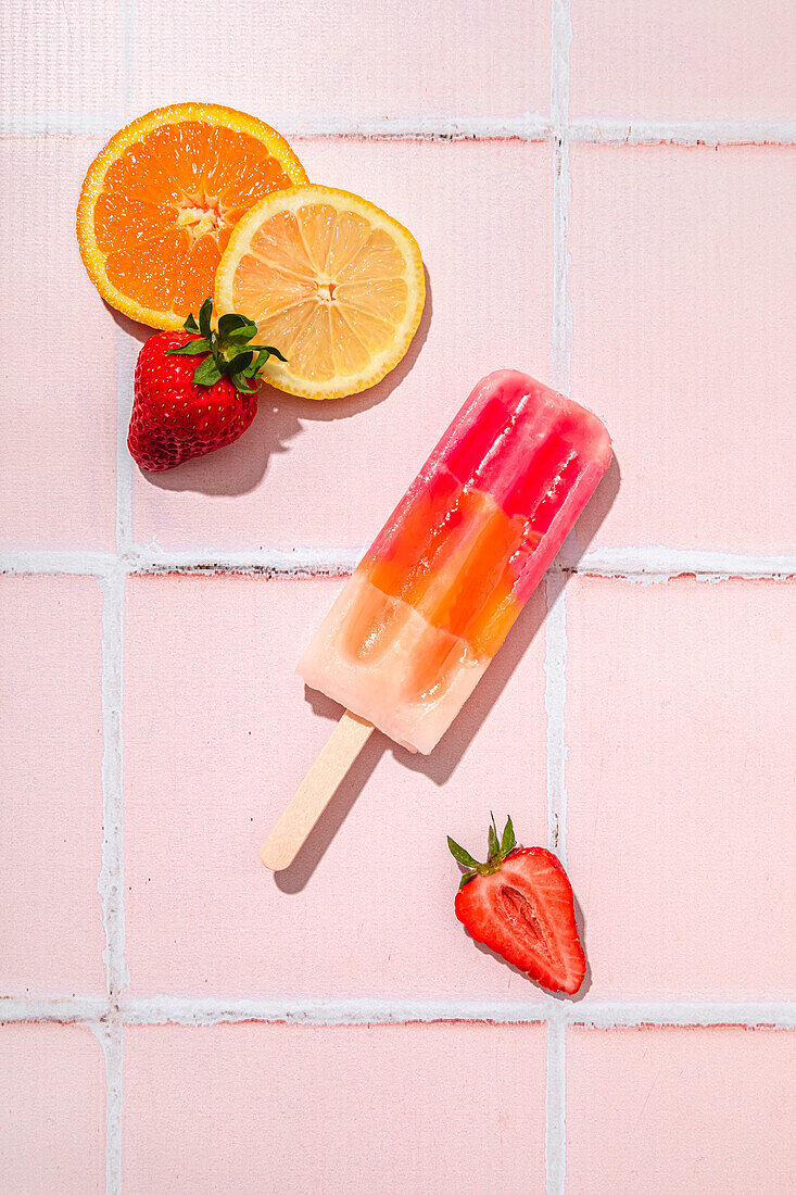 Fruit popsicle with ingredients on a pink tiled background
