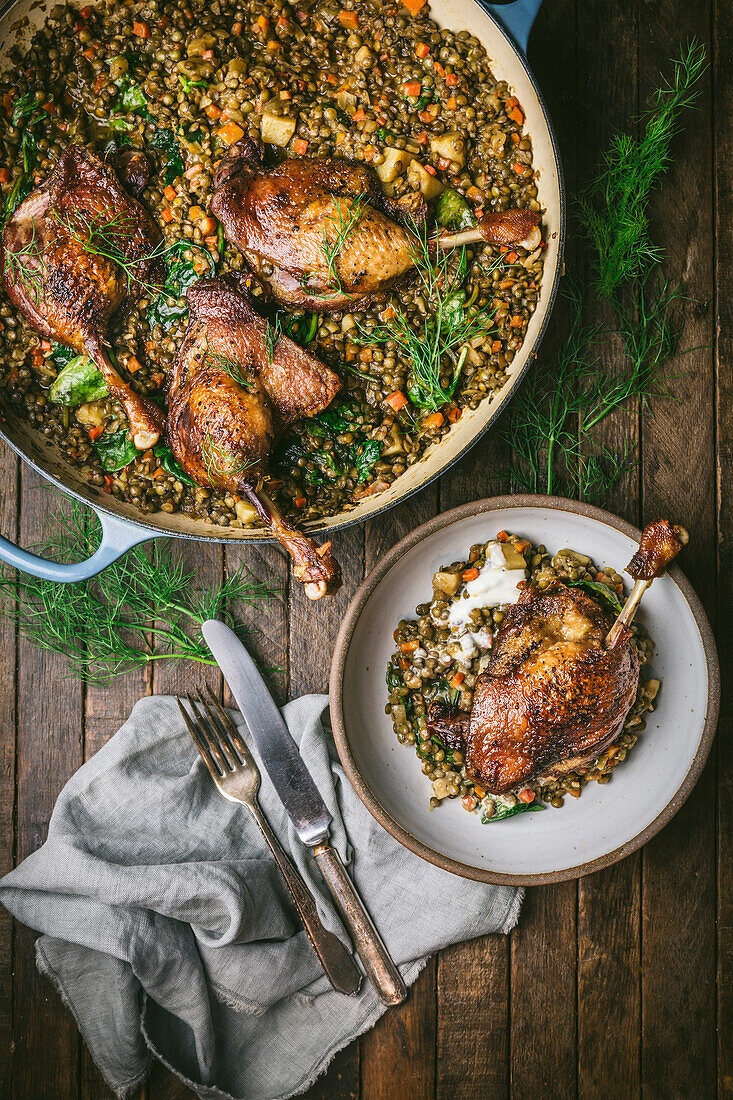 Duck legs on lentils in a casserole and serving bowl with crème fraiche