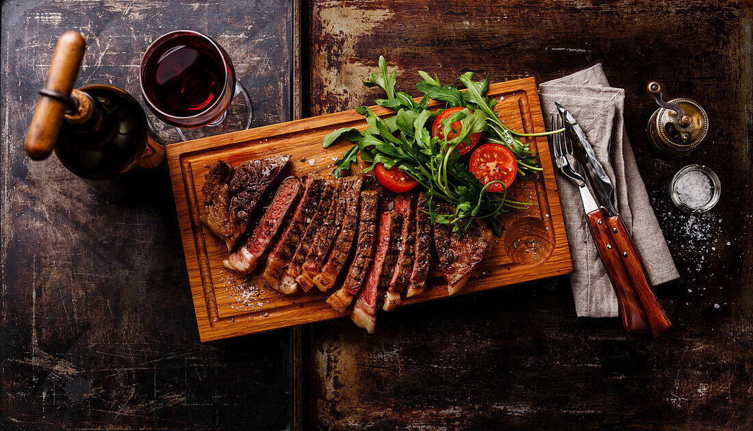 Grilled beef striploin steak with rocket salad and red wine on a dark background