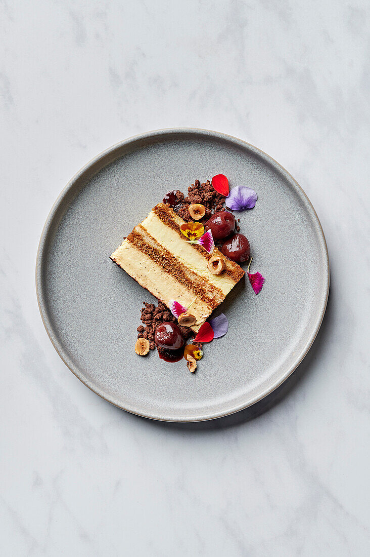 A slice of tiramisu with spiced cherry compote, salted chocolate sprinkles and candied hazelnuts