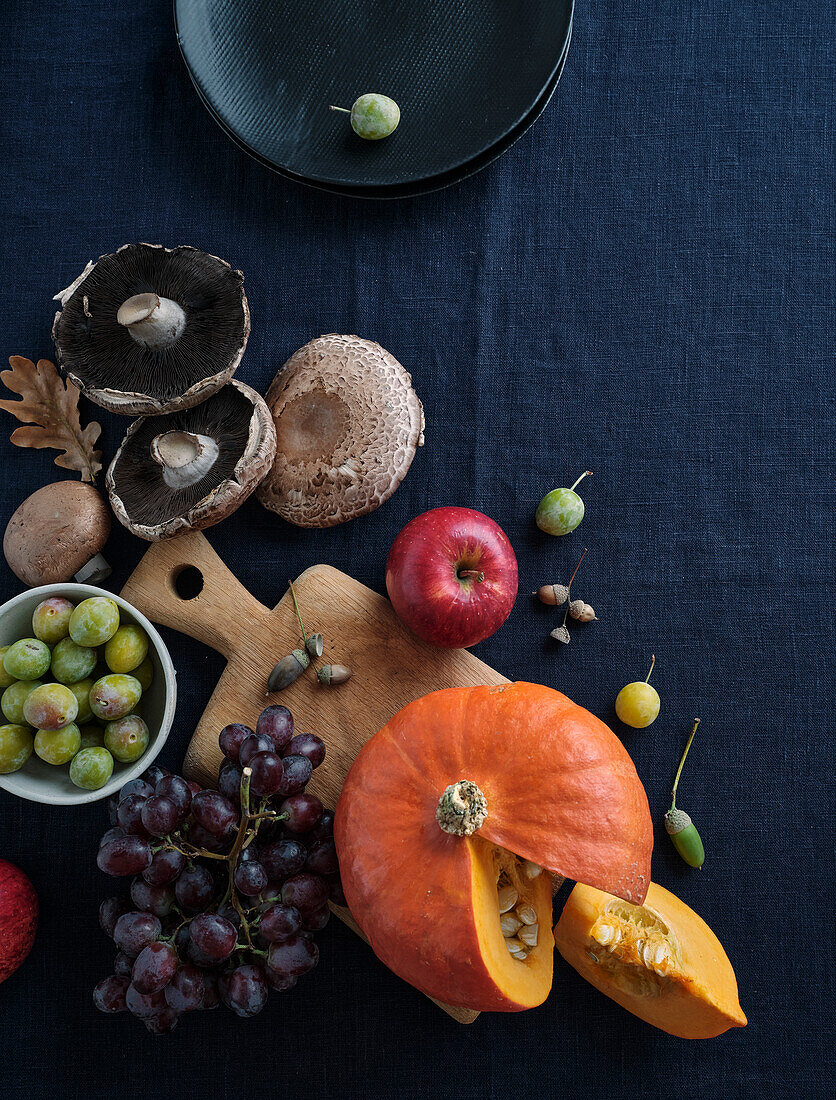 Herbstliche Lebensmittelzutaten auf dunkelblauem Hintergrund mit Kopierraum. Flat-Lay von Herbstgemüse, Beeren und Pilzen vom lokalen Markt. Vegane Zutaten