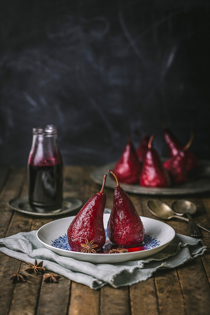 Pears poached with red wine on a white and blue plate with pears in the background