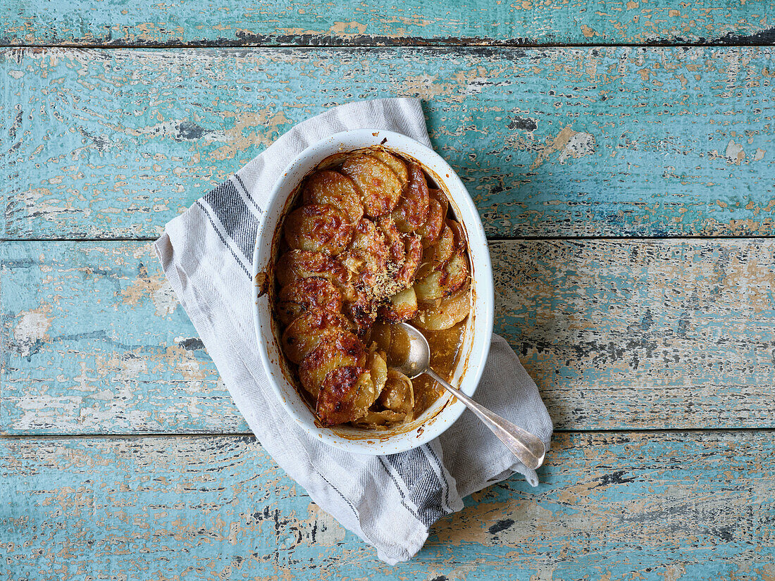 Kartoffelgratin in weißer Auflaufform von oben auf hölzernem Hintergrund mit Kopierraum