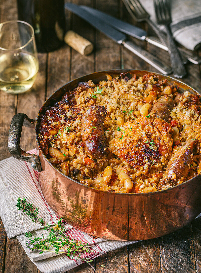 Classic French cassoulet with chicken and sausage in antique copper pot with wine glass and bottle