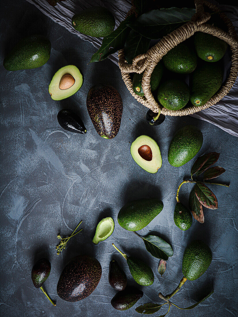 Schwarze und grüne Avocados in einem Korb und auf einem Tisch