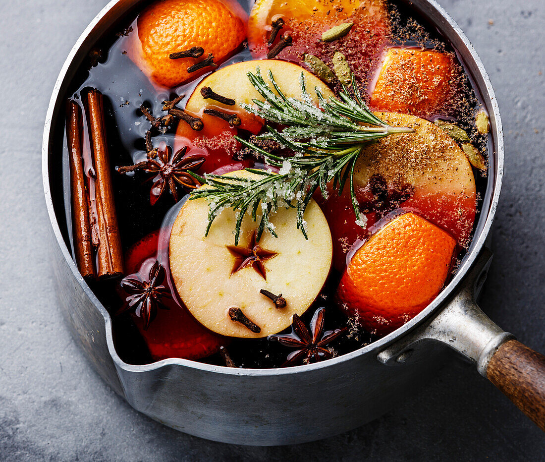 Mulled wine hot drink with citrus, apple and spices in aluminum casserole and rosemary sugar close-up