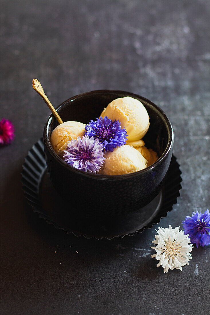 Scoops of vanilla ice cream with edible flowers in a dark bowl