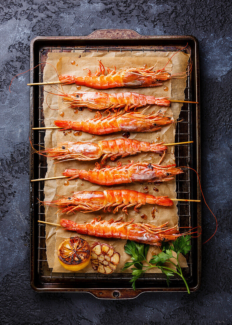 Grilled fried prawns Langostino Austral on skewers on metal grid baking tray on black background