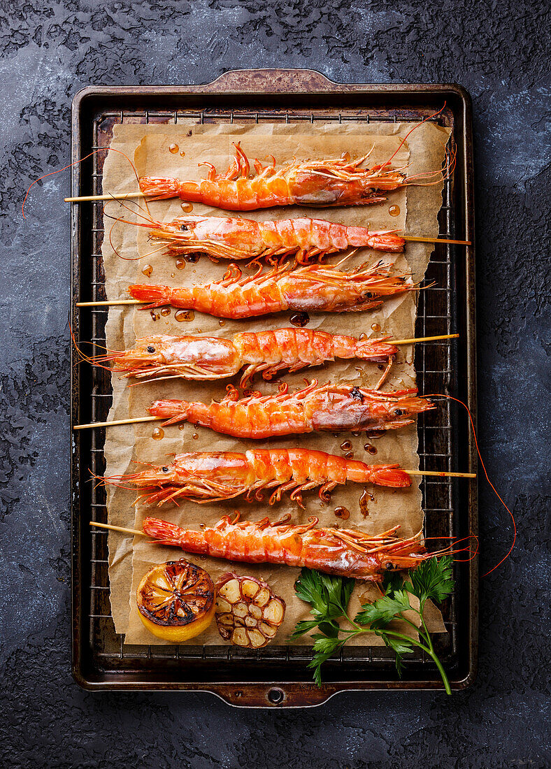 Grilled fried prawns shrimps Langostino Austral on skewers on metal grid baking sheet on black background