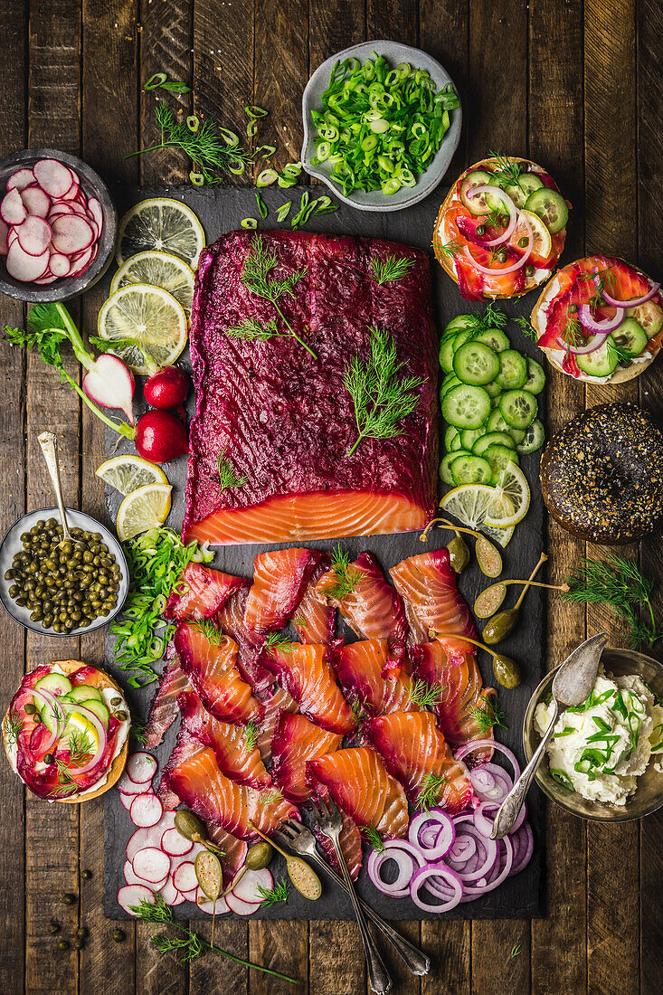 Brunch spread with beetroot salmon, bagels, cream cheese and trimmings on a slate plate