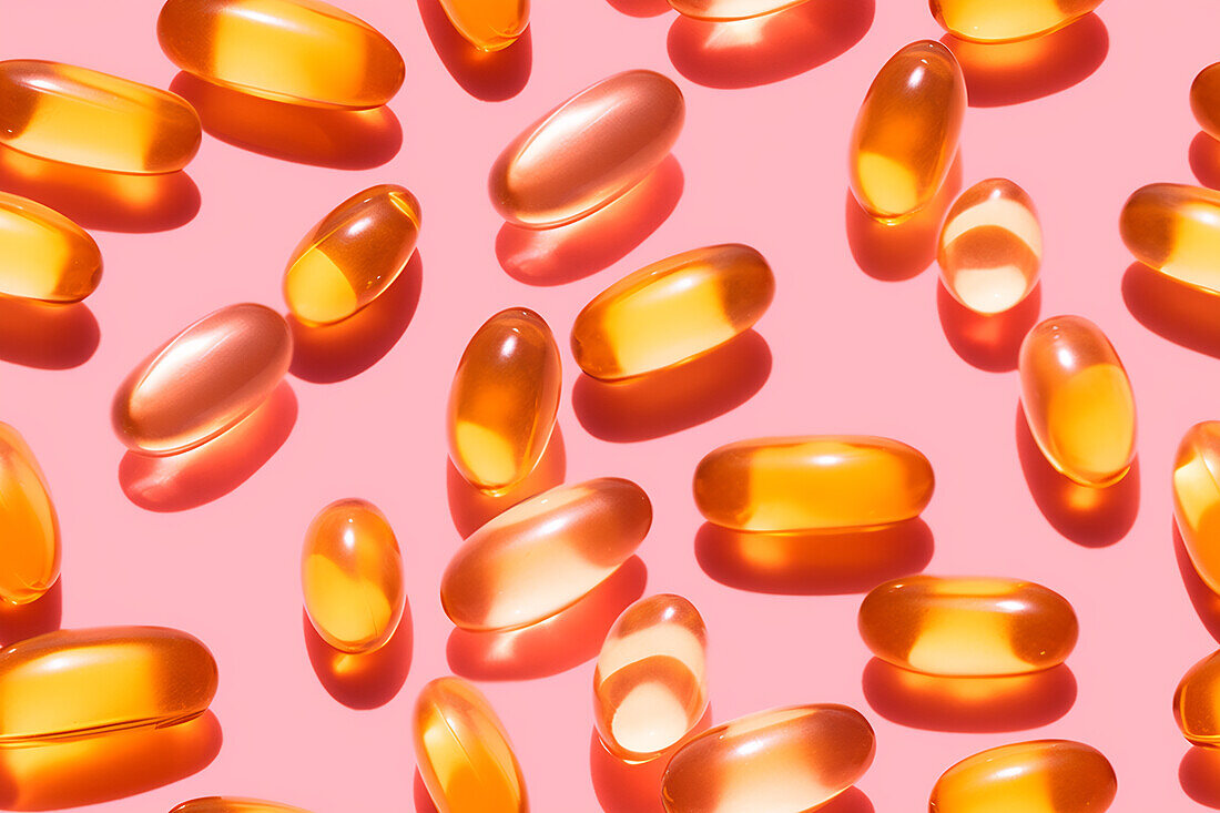 Assortment of orange-coloured vitamin pills scattered on a pink background in a bright studio