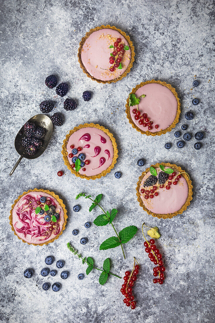 Arrangement of four small tarts filled with berry cream, decorated with fresh fruit and mint