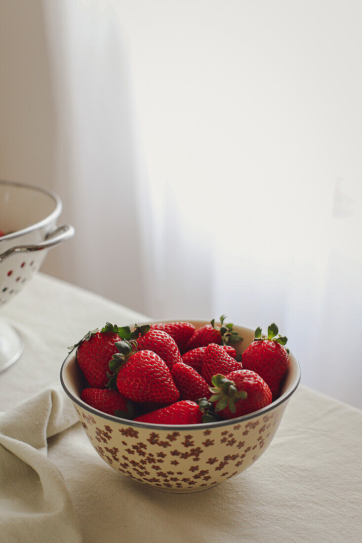 Schale mit Erdbeeren auf einem Tisch neben einem Fenster