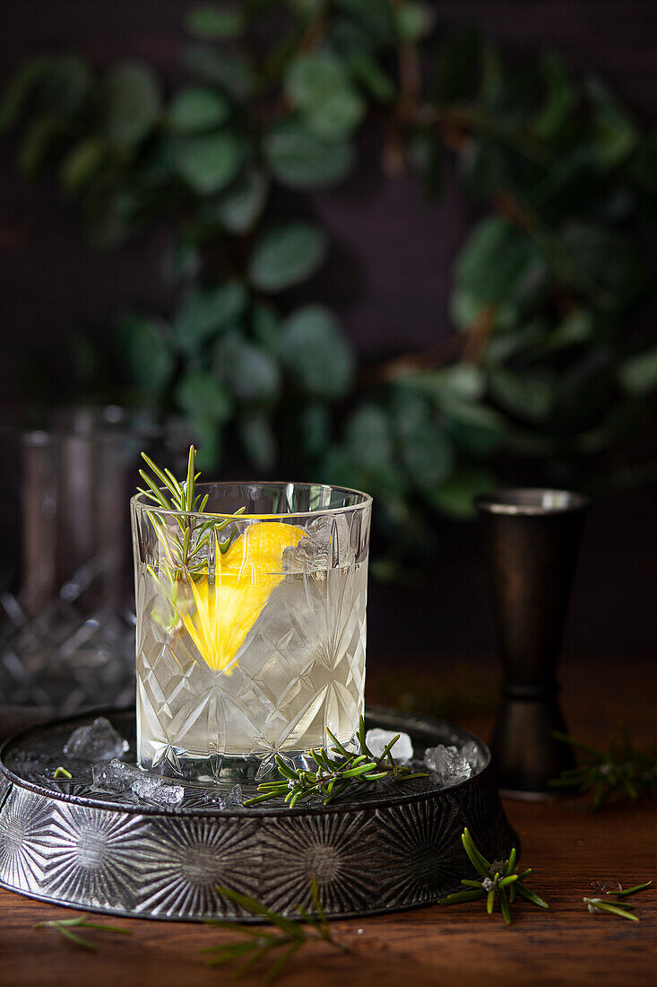 A gin cocktail in a tumbler served with a lemon and rosemary garnish.