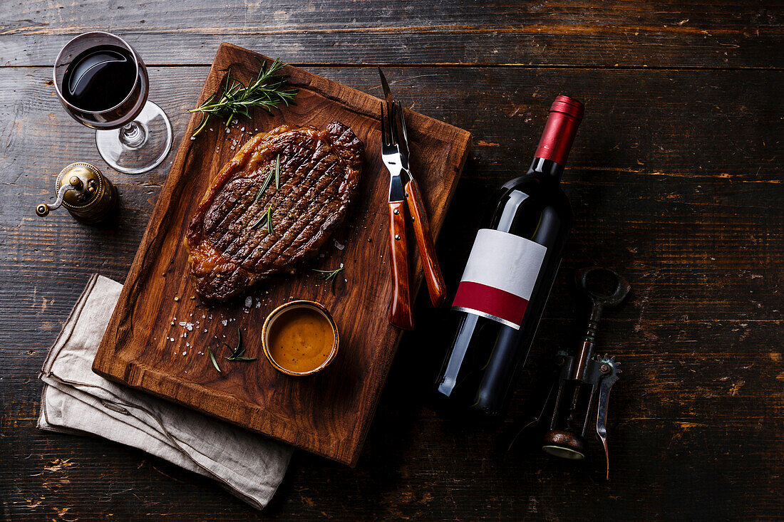 Grilled steak rib eye with pepper sauce and a bottle of red wine on a wooden base