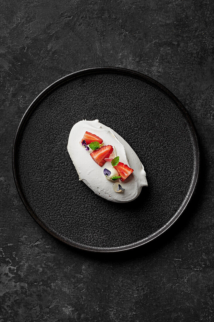 Meringue with yoghurt mousse, macerated strawberries and bergamot gel from above on black plate