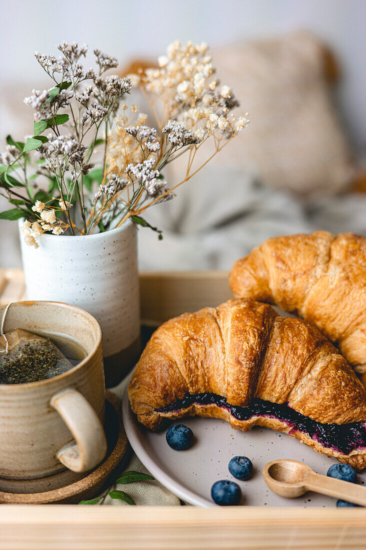 Breakfast in bed with freshly baked croissants with blueberry jam and tea in a mug